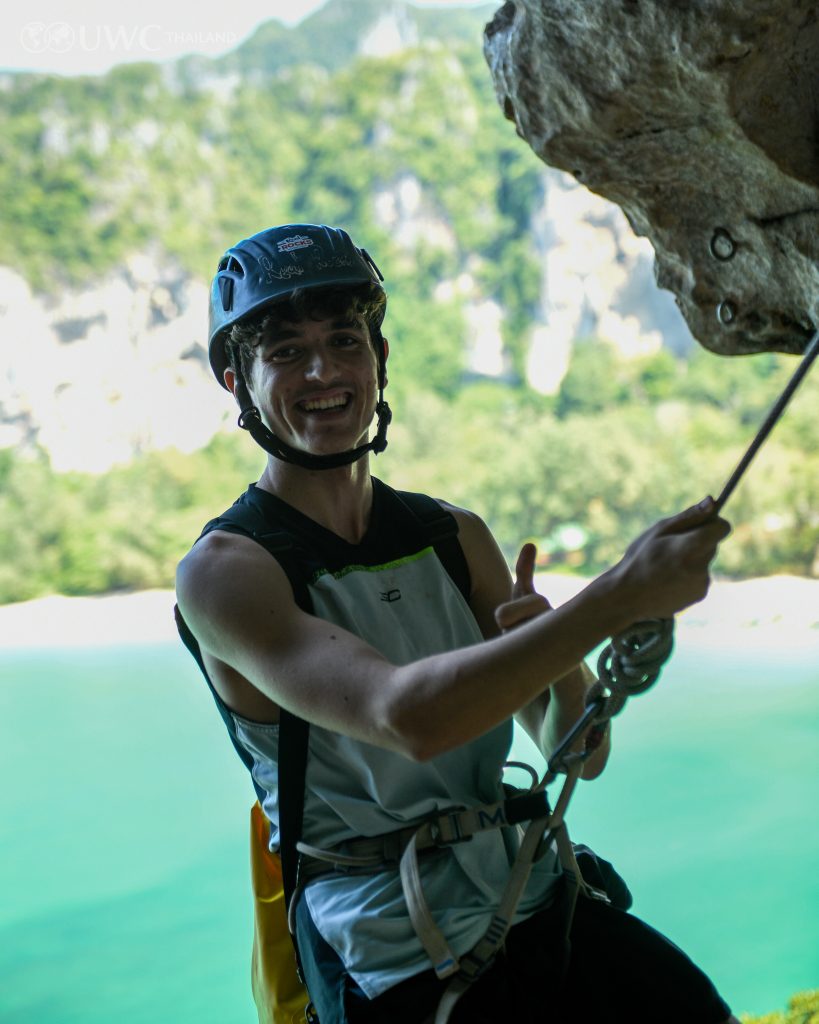 Student climbing up rock face giving a thumbs up